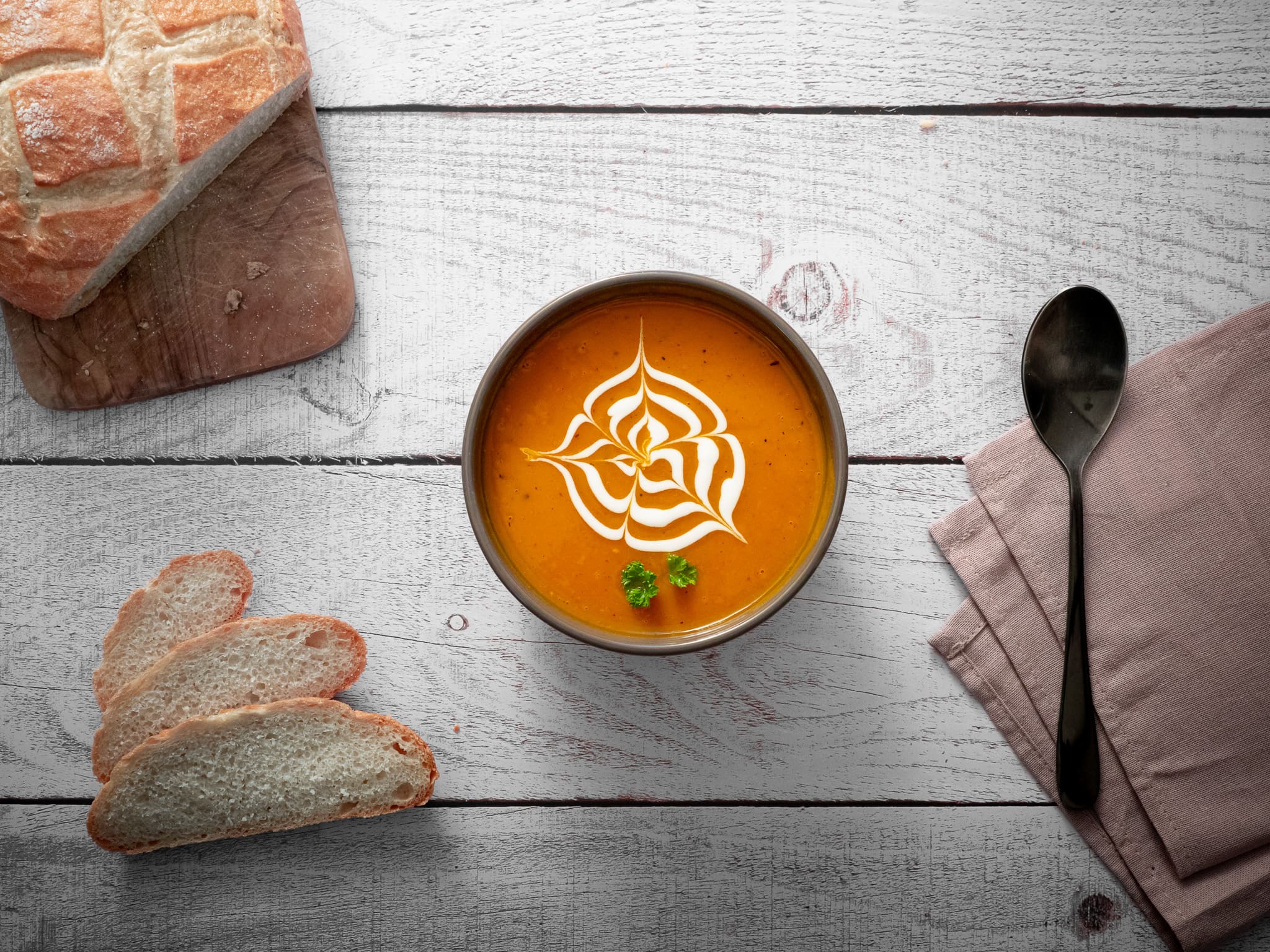 un bol de soupe de potimarron avec du lait de coco du persil et trois tranches de pain sur une table en bois
