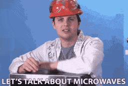 un homme avec une blouse un casque et des lunettes s'appuie sur un micro ondes et dit let's talk about microwaves