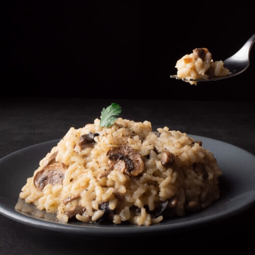 assiette de risotto aux champignons de Paris avec une fourchette au-dessus qui s’apprête à être dégustée