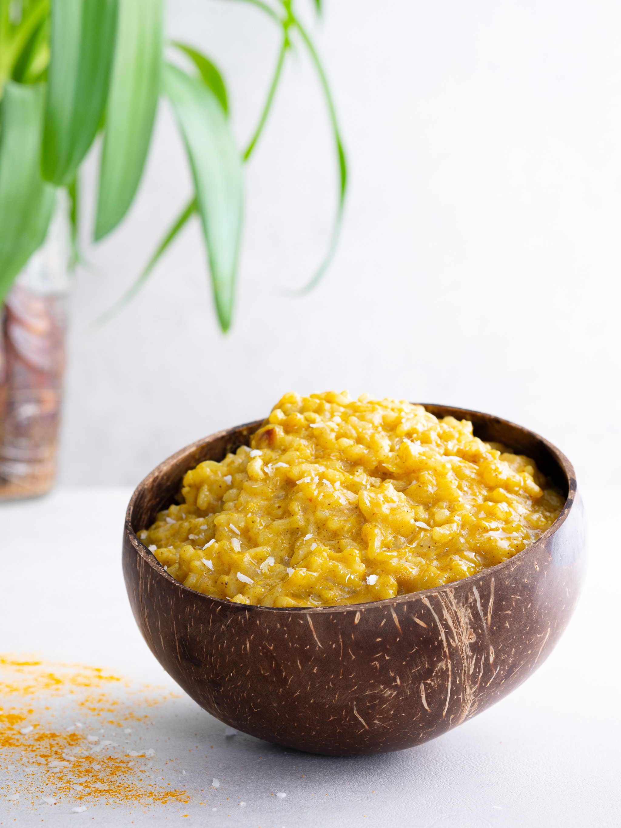 risotto curry coco vegan dans un bol en coco et quelques copeaux sur la table dans une ambiance exotique