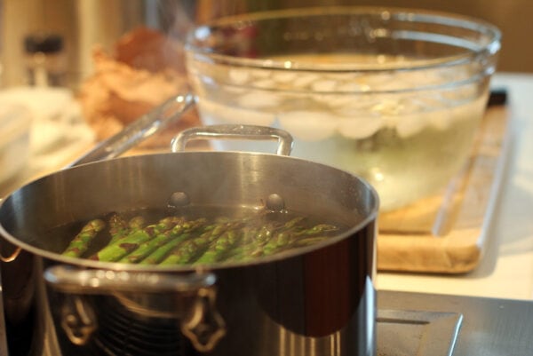 des asperges vertes dans de l'eau bouillante prêtes à être plongées dans un saladier d'eau glacée