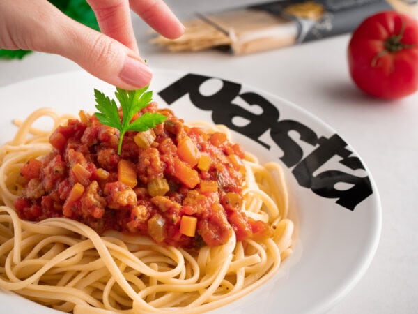 marion dépose une feuille de persil sur un plat de spaghetti bolognaise dans une assiette à pâtes