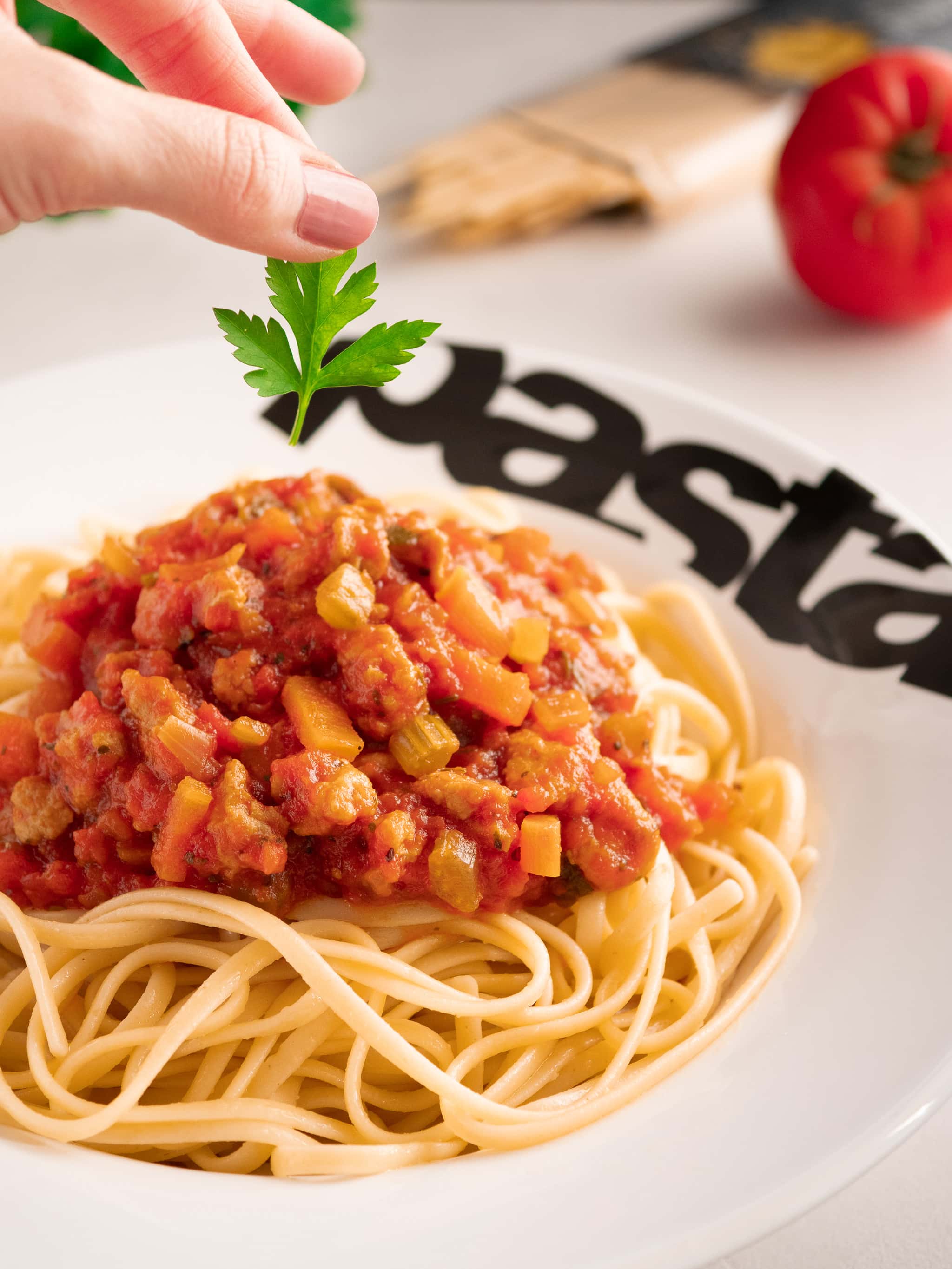 marion dépose une feuille de persil sur un plat de spaghetti bolognaise dans une assiette à pâtes