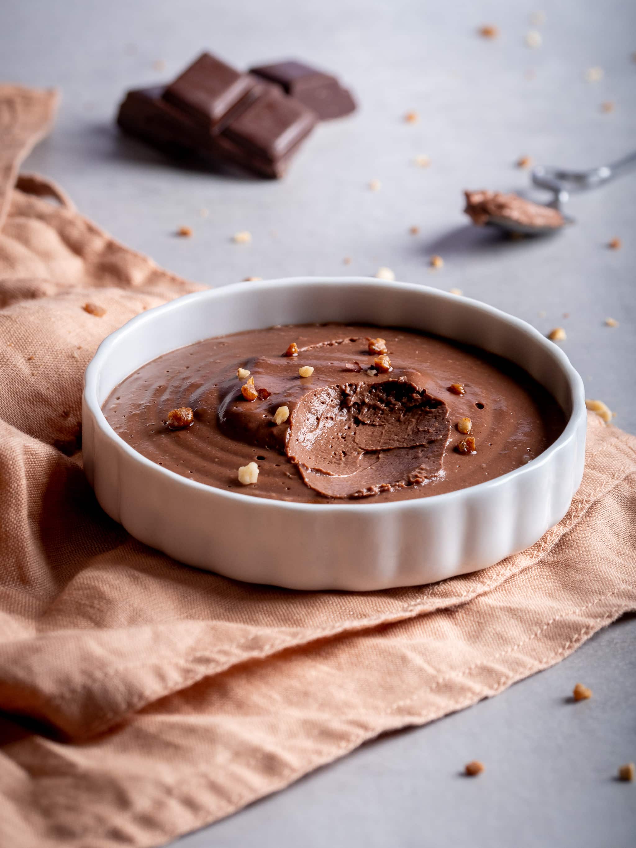 une crème chocolat noisettes vegan au tofu soyeux servie avec du pralin et quelques carrés de chocolat