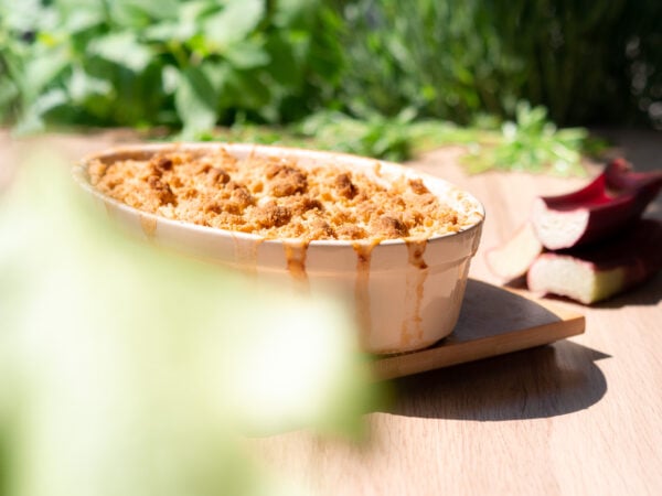 un plat de crumble pomme rhubarbe vegan est posé sur une table en bois lors des premiers jours de soleil du printemps