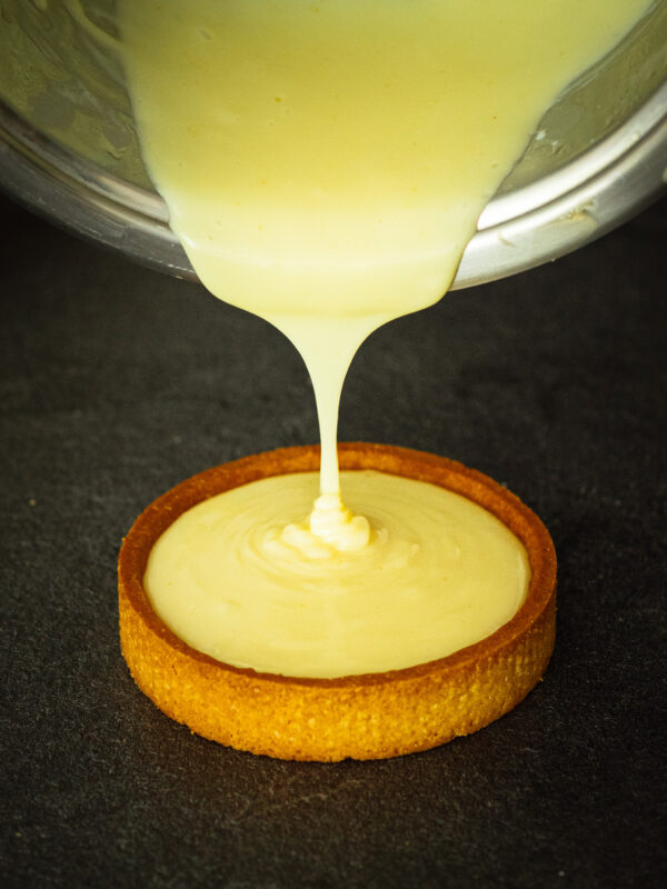 une crème pâtissière vegan aromatisée au citron est versée dans un fond de tarte en pâte sablée vegan