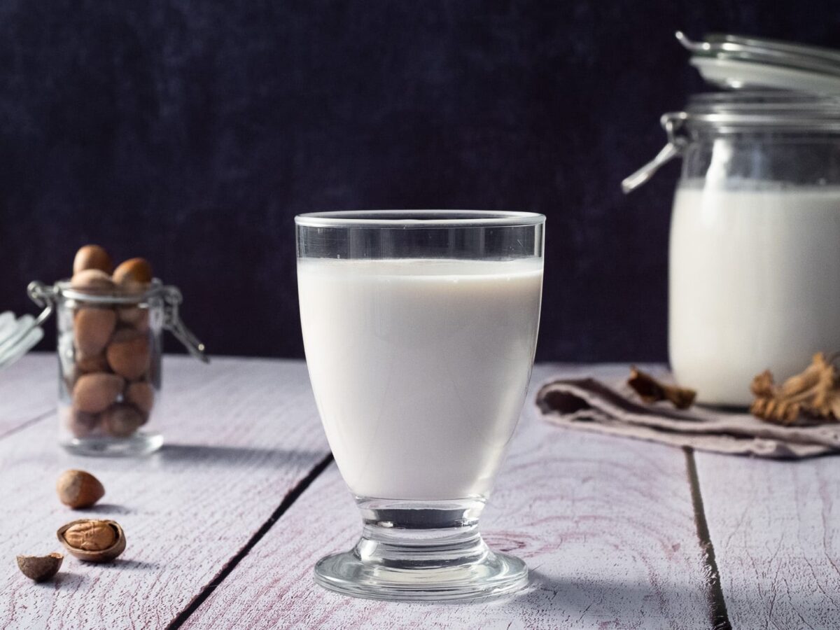 un verre de lait de noisettes maison avec un bocal de noisettes et une bouteille de lait végétal en arrière plan