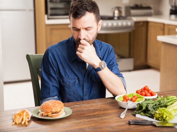 un homme hésite entre un burger avec de la viande et un repas végétal