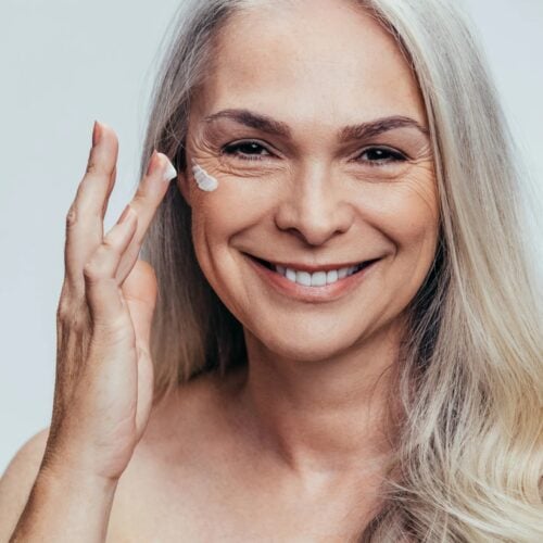 une femme au cheveux blanc et souriante s'applique un masque anti-âge à base de spiruline
