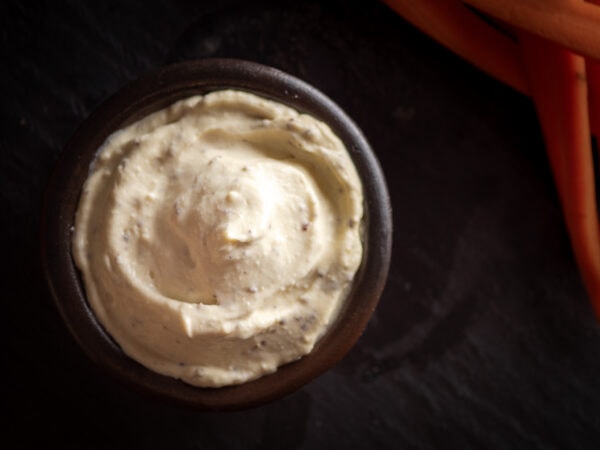 mayonnaise vegan maison à la moutarde à l'ancienne servie dans un bol avec des bâtonnets de carotte