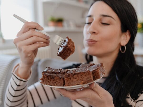 une femme mange un gros gateau au chocolat avec une expression de bonheur