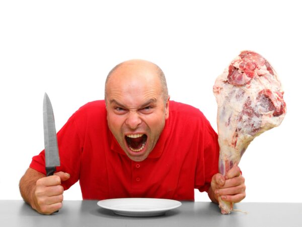 un homme énervé, tenant un couteau dans une main et un gros morceau de viande dans l'autre